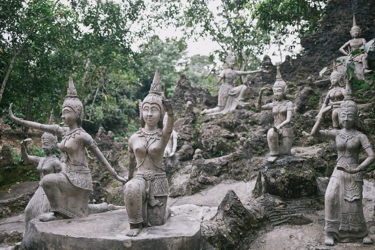 Une sculpture en pierre dans le Parc de Sculptures Hikulagi, partiellement dissimulée par des lianes et fougères tropicales