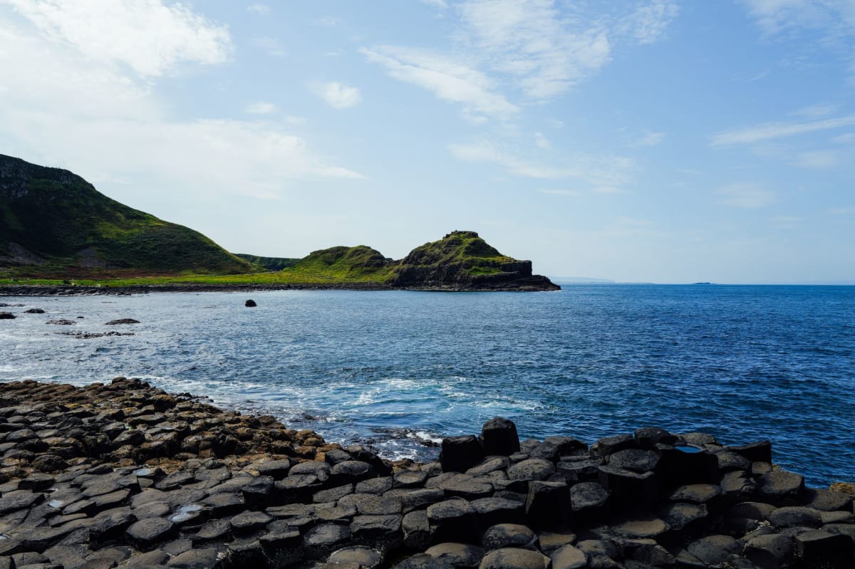 El puente de cuerda visto desde el lado de la isla, con el acantilado de la costa de Antrim y el camino más allá, luz atlántica derramándose a través de un hueco en las nubes