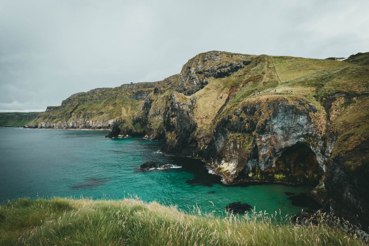 Puerto de Ballintoy desde arriba, edificios encalados curvándose alrededor de la ensenada rocosa, barcas de pesca en reposo en agua baja sobre roca natural
