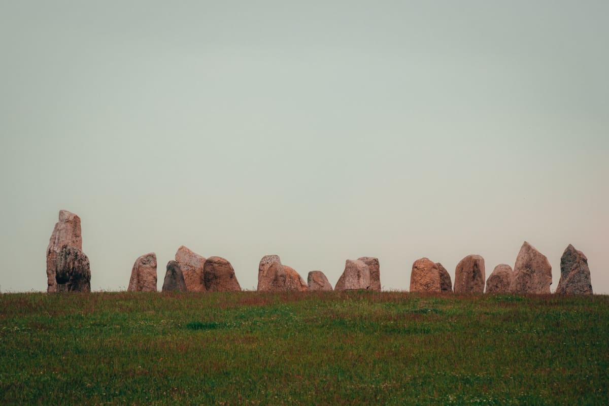 Las piedras del Círculo de Brodgar recortadas contra un cielo pálido de tarde, las aguas del Lago de Harray detrás de ellas