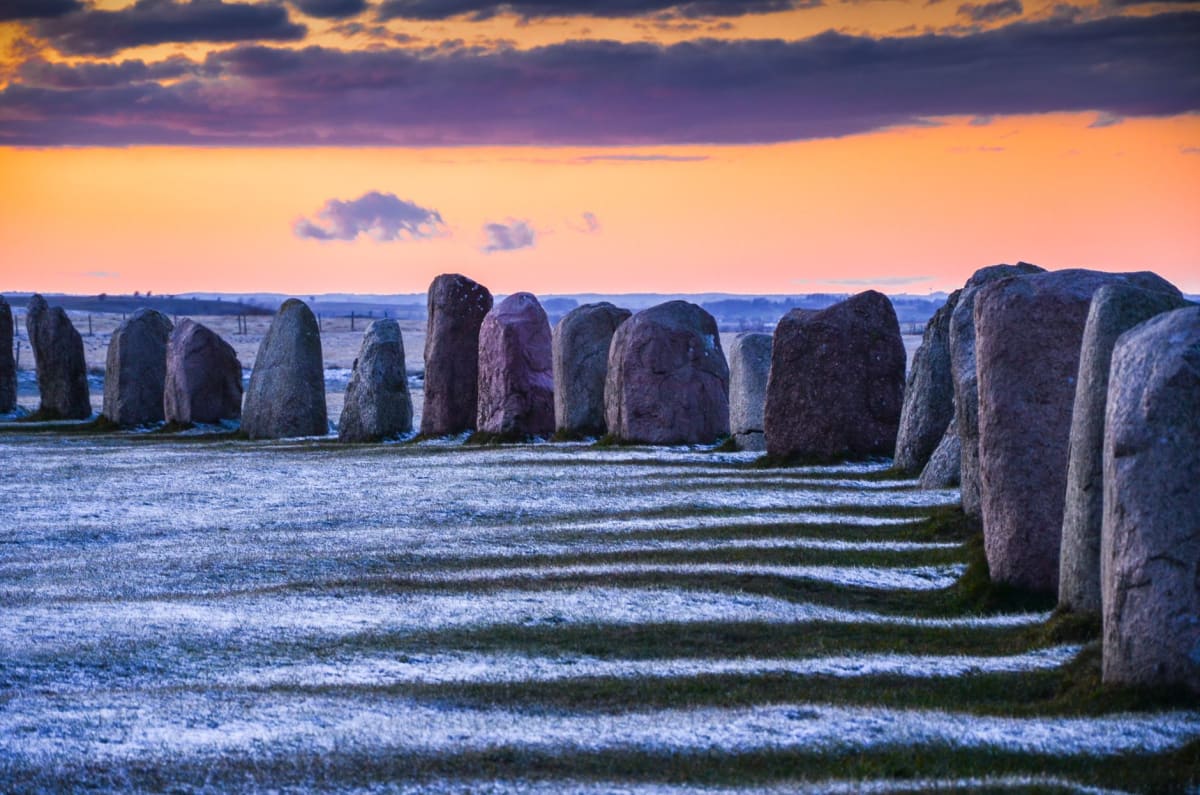 El foso del Círculo de Brodgar cortado en el páramo de brezo con las piedras emergiendo de él, el lago al fondo