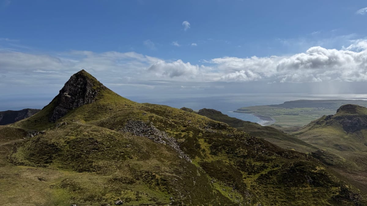 La rue courbe de maisons de pierre sans toit dans le village abandonné de St Kilda, avec la colline verte et les cleitean derrière