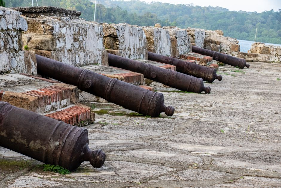 A row of old Spanish cannons still positioned along the mossy stone ramparts of Fuerte Santiago above Portobelo bay