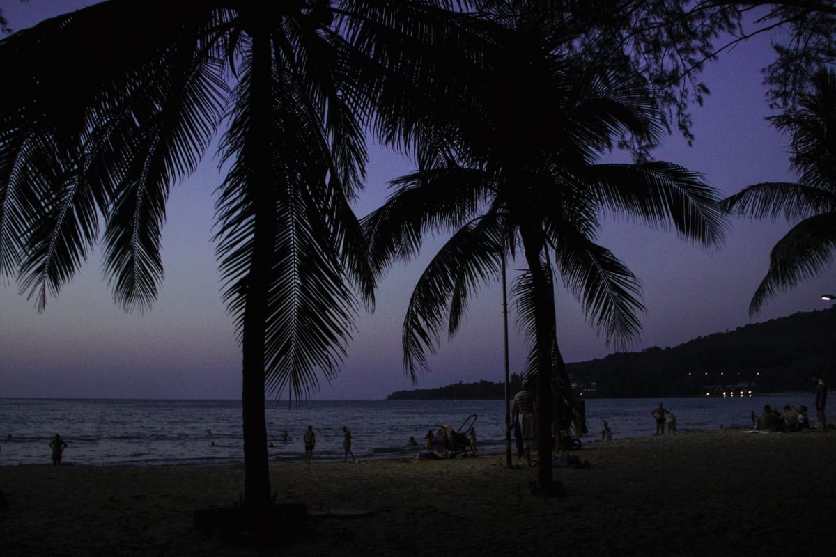 Karon Lake in the evening, Thai families walking the path around it, the Andaman visible through the palms beyond