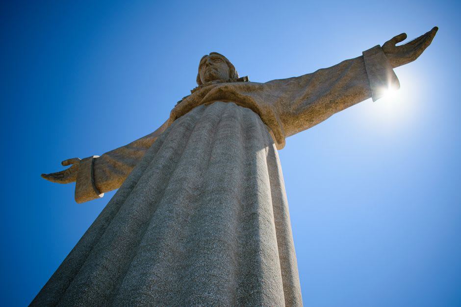 La estatua del Cristo Rei en Almada con los brazos extendidos sobre el río Tejo y el perfil de Lisboa