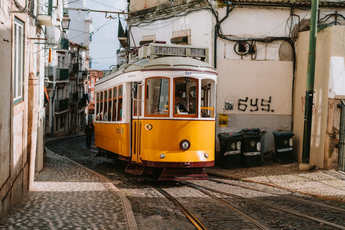 Colorful tiled buildings along a narrow Lisbon street with the yellow tram