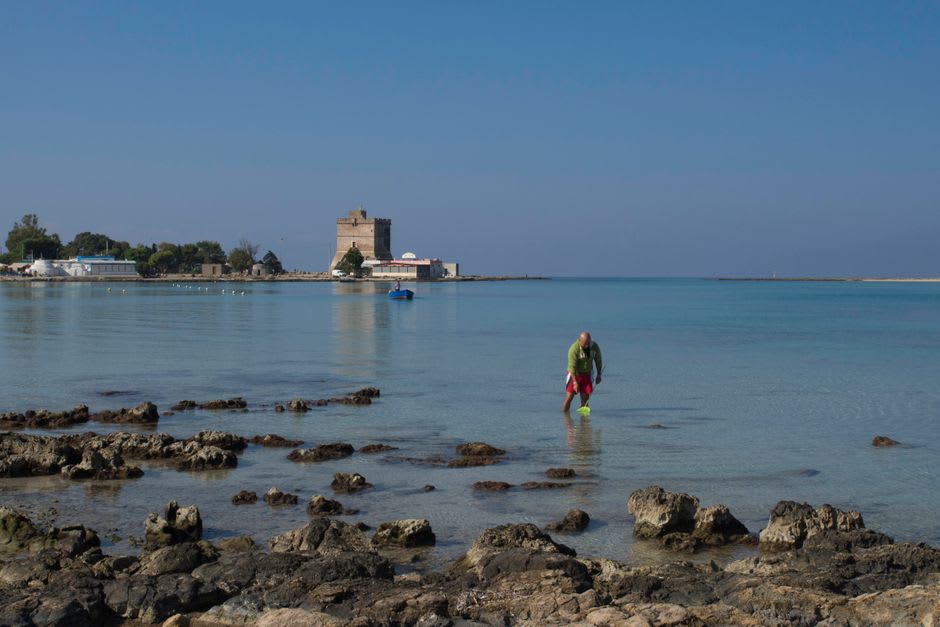 La arena a la sombra de los pinos en la playa de Torre dell'Orso con los peñascos gemelos Due Sorelle visibles frente a la costa
