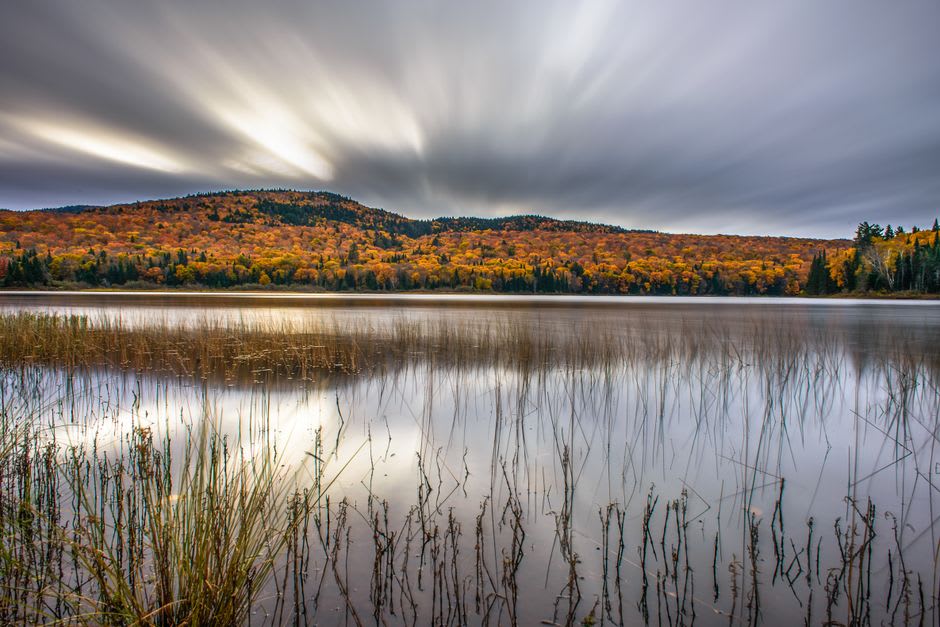 A canoe pulled up on the shore of Lac Monroe in Parc national du Mont-Tremblant, forested hills rising behind under a clear sky