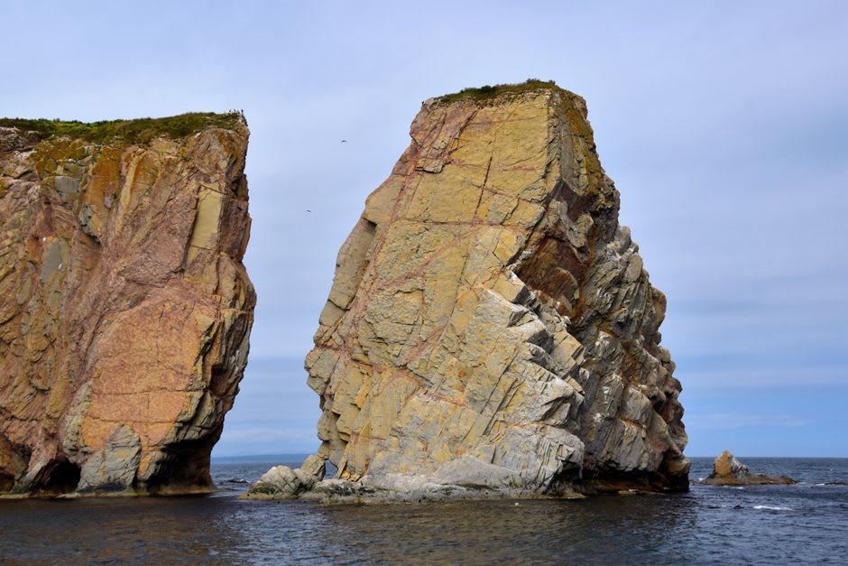 El pueblo de Percé a la hora dorada con Rocher Percé brillando en tonos rosa y oro mar adentro y botes de pesca en el puerto en primer plano