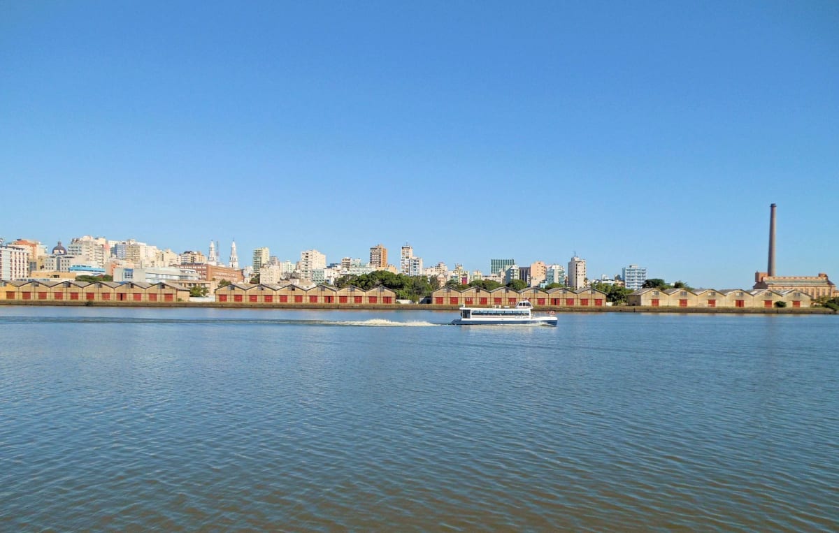 Des gens rassemblés sur le front du Guaíba à l'heure dorée, le fleuve brillant en orange et violet