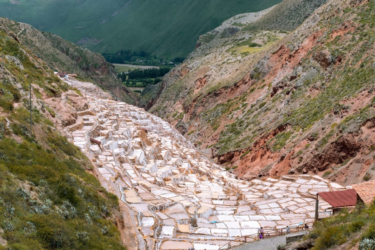 Salineras de Maras con luz de tarde, pozas que van del blanco brillante al ámbar, un trabajador solitario visible a lo lejos