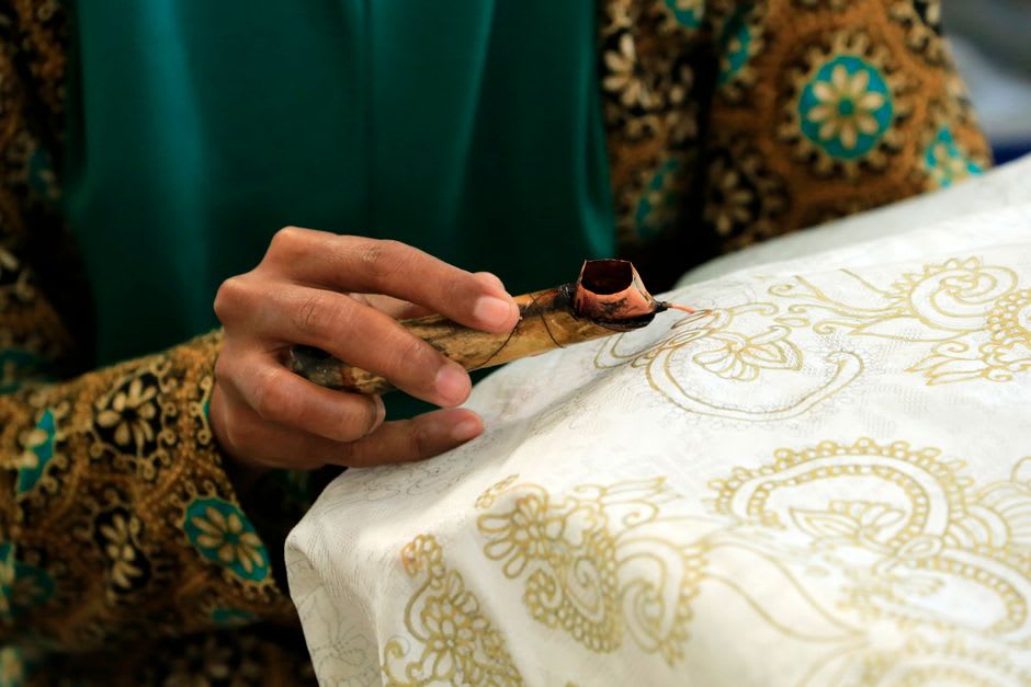 Una artesana de batik en Romney Manor aplicando patrones de cera sobre tela con una herramienta tjanting tradicional
