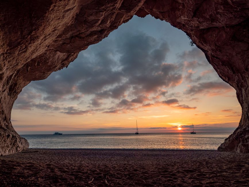Un barco aproximándose a la playa en media luna de Cala Luna entre imponentes acantilados calizos en el golfo de Orosei de Cerdeña