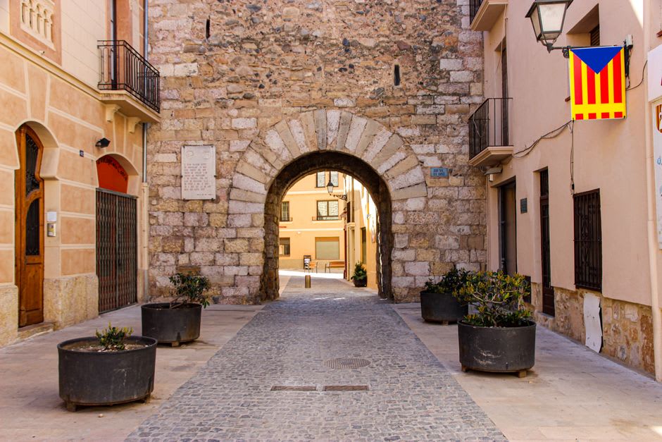 Un arco de piedra desgastado que da acceso al casco antiguo de Chinchón, con ristras de ajos colgando de un escaparate cercano