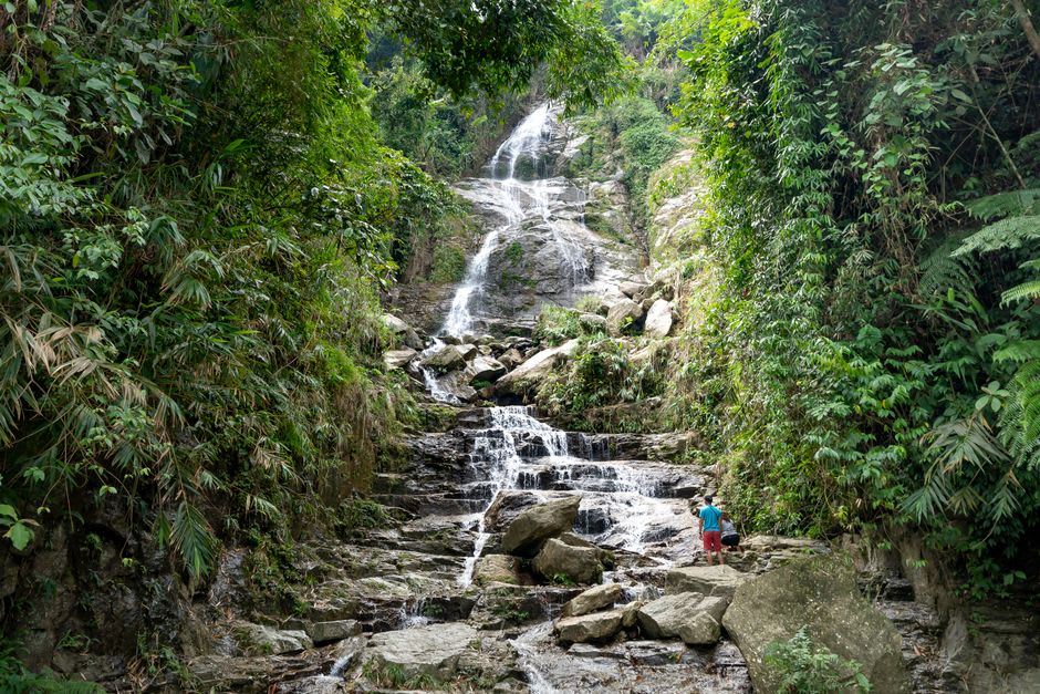 Excursionistas vadeando un arroyo de selva hacia una cascada de varios niveles