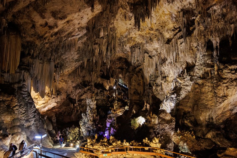 Small limestone cave passage lit by a ranger's lantern with visible stalactites