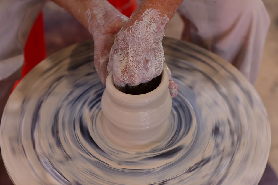 Potter's hands shaping clay on a spinning wheel in a Gijduvan workshop