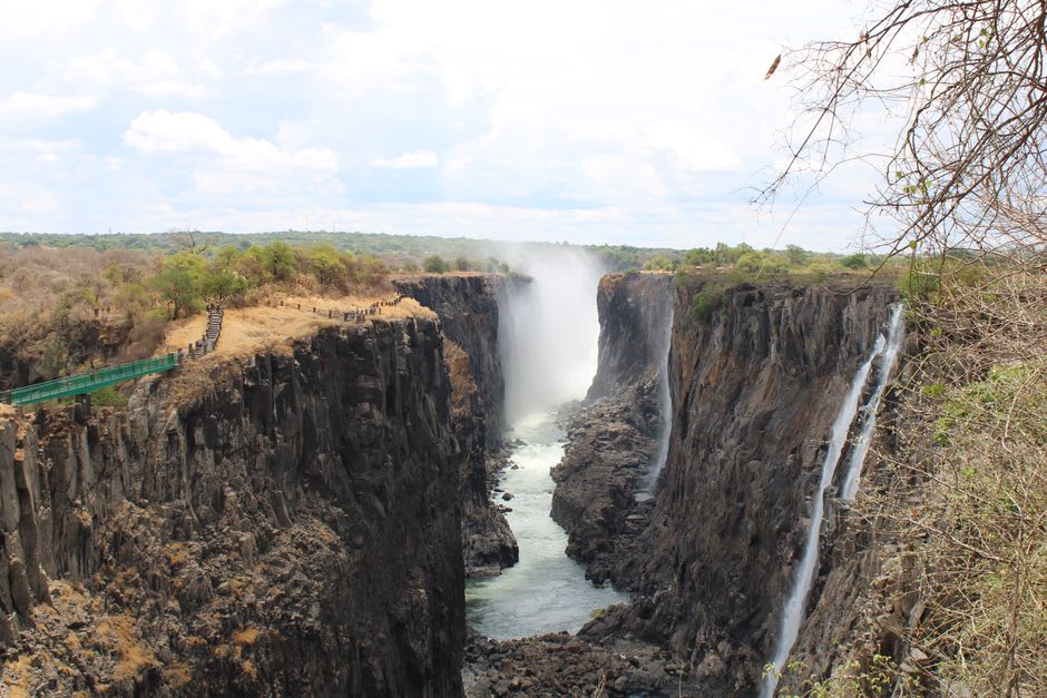 Hikers crossing a narrow steel footbridge engulfed in falls spray