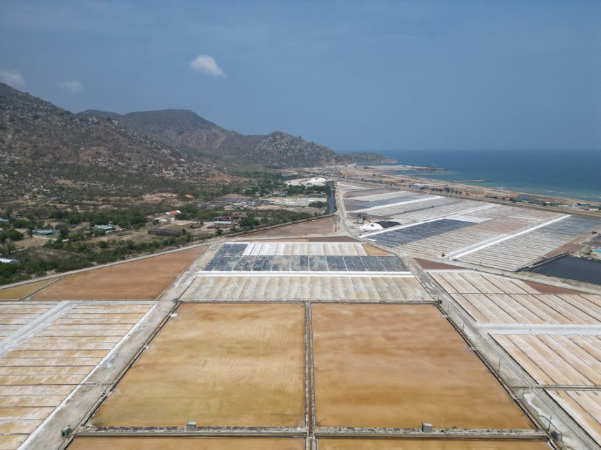 Aerial-style view of white salt mountains stacked beside pink saline pools