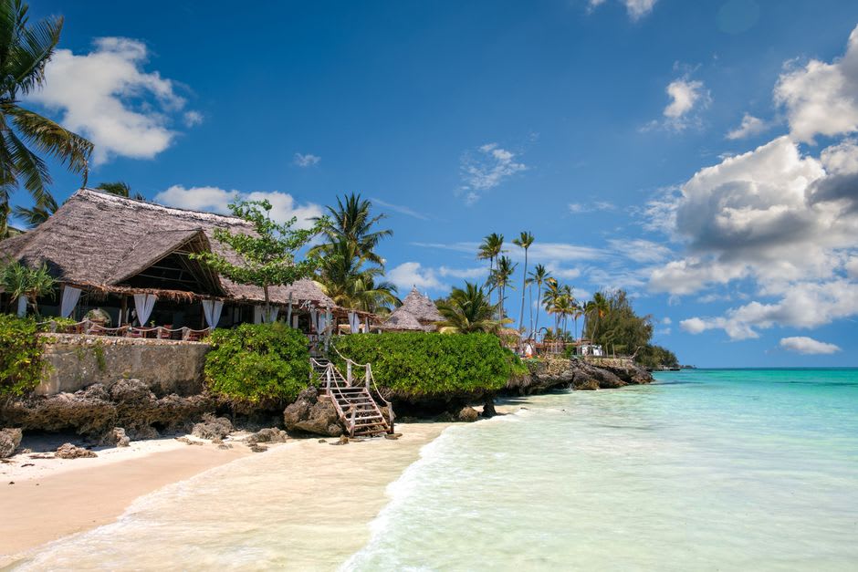 Idyllic beachfront in Zanzibar with palm trees framing turquoise Indian Ocean water and a traditional villa on the shore