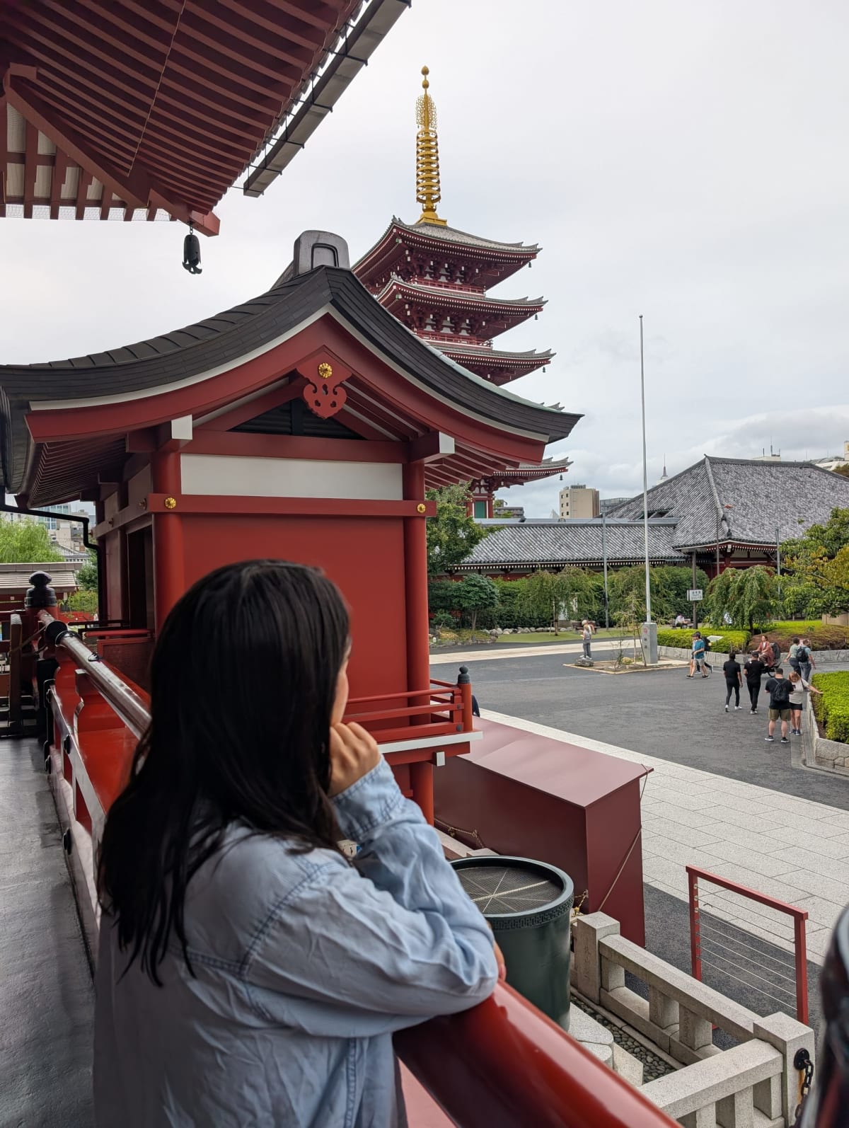 Lia leaning on a red railing at Senso-ji, looking out at the five-story pagoda over the rooftops of the temple complex