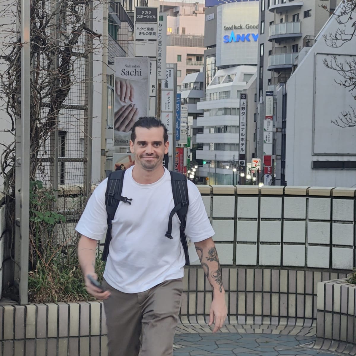 Pierre smiling for a photo on a Ueno backstreet, office and salon signage crowding the buildings behind him