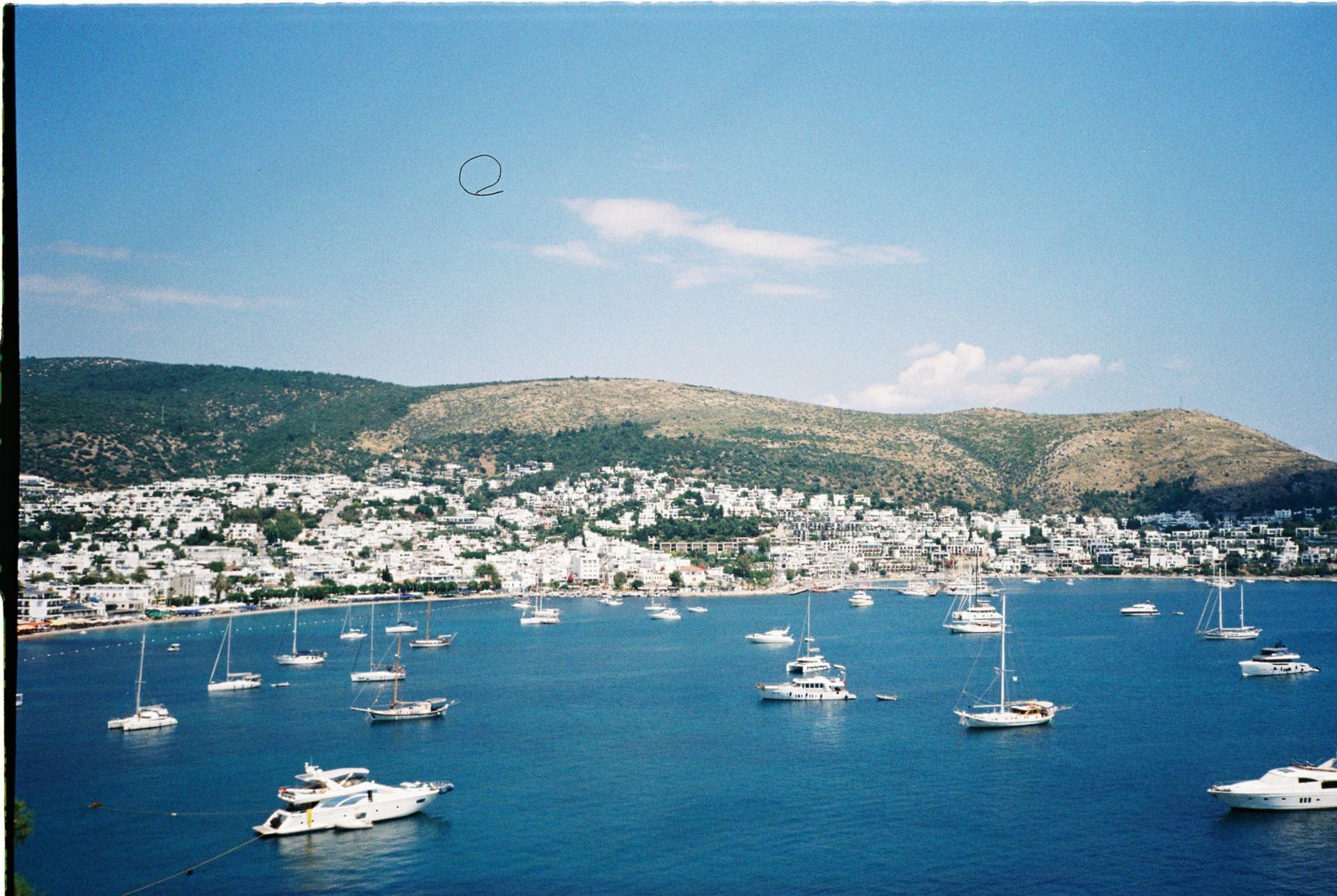 Bodrum's coastline on a sunny day with white buildings cascading toward a harbor full of yachts