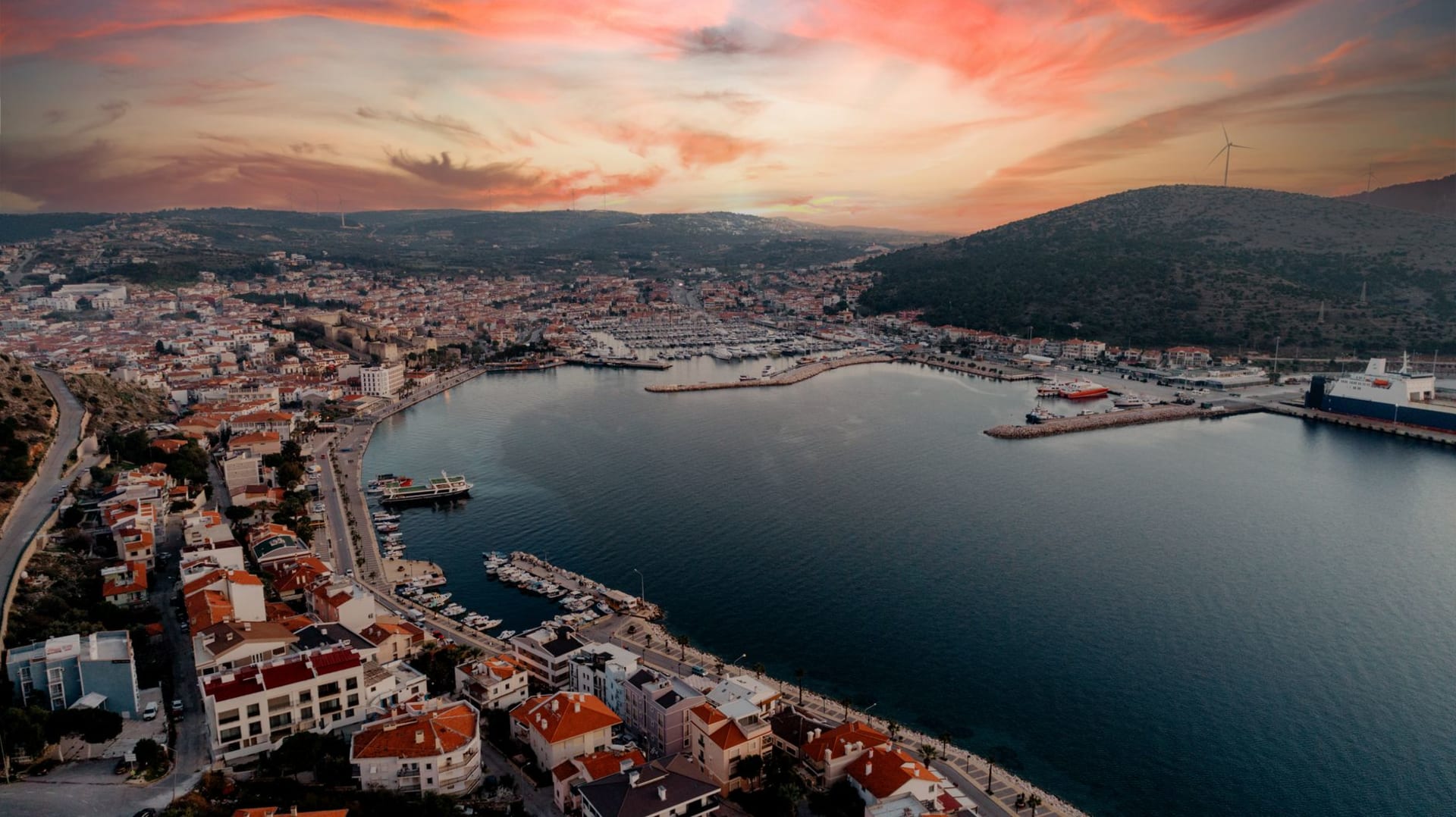 Le château et le port de Çeşme au coucher du soleil, des bâtiments blancs descendant vers le front de mer avec Chios visible à l'horizon