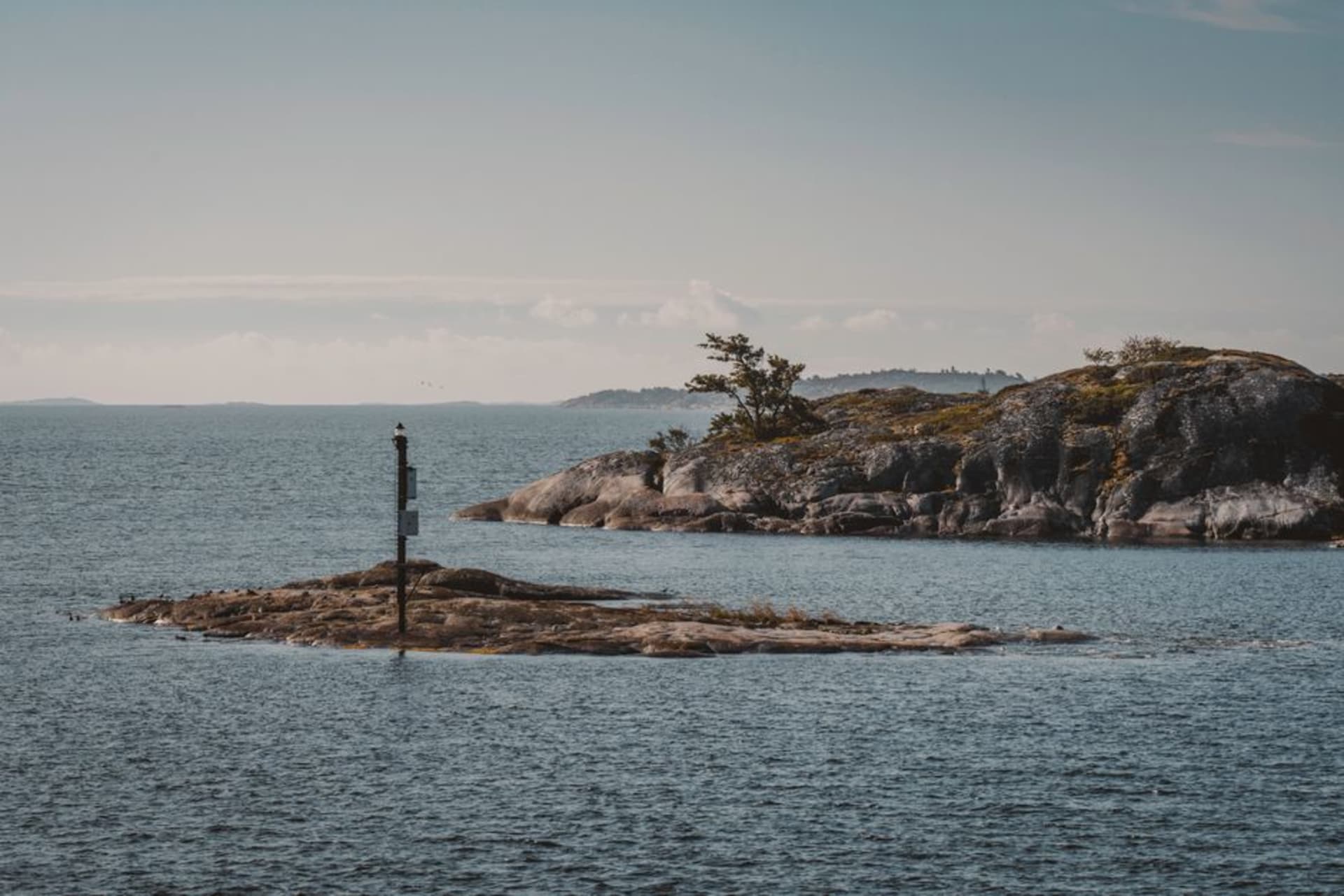 Small red and white ferry crossing calm water between low pine-covered islands in the eastern Åland archipelago