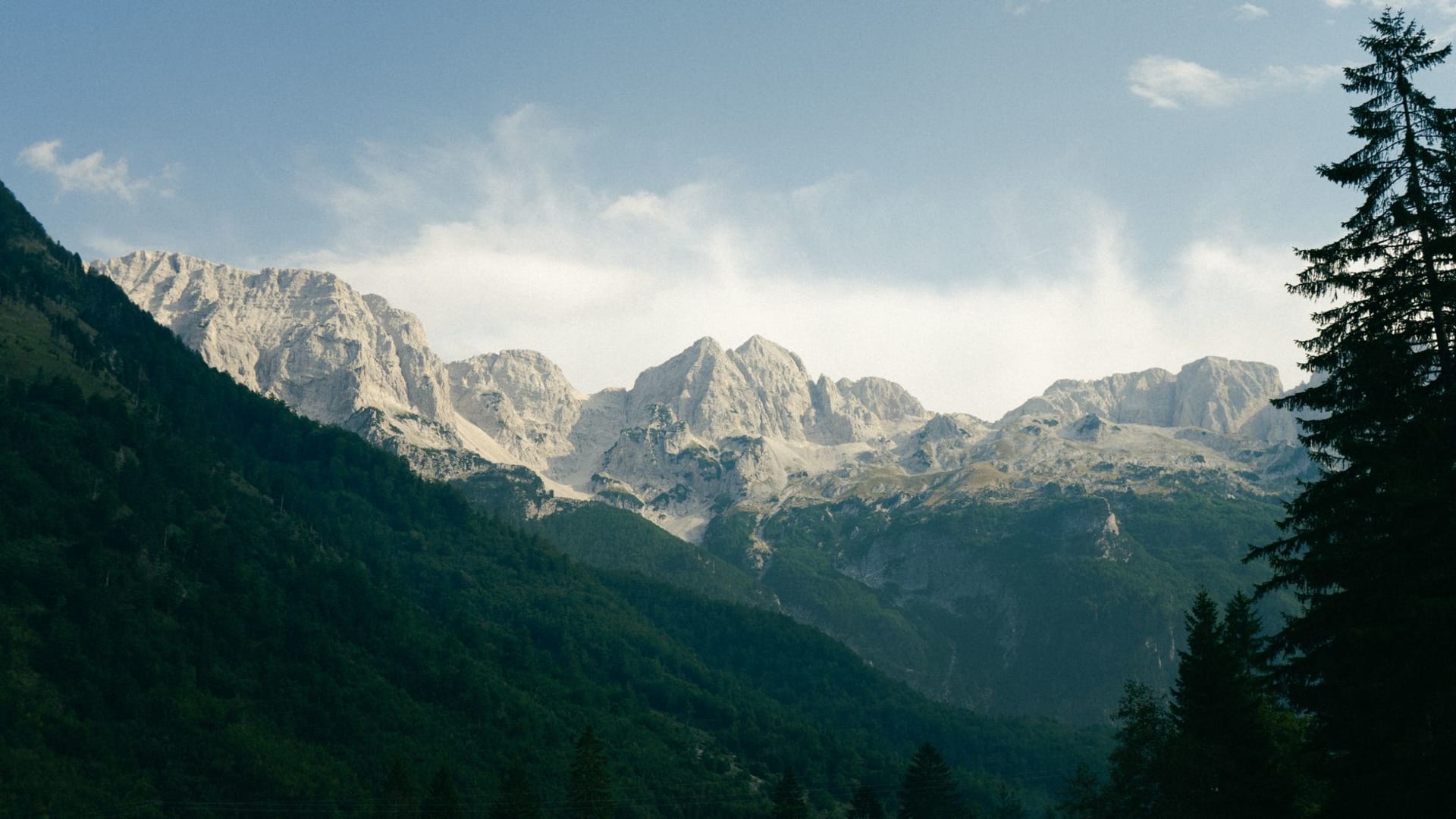 Turquoise Valbona River cutting through a wide valley floor ringed by jagged grey peaks under sharp morning light