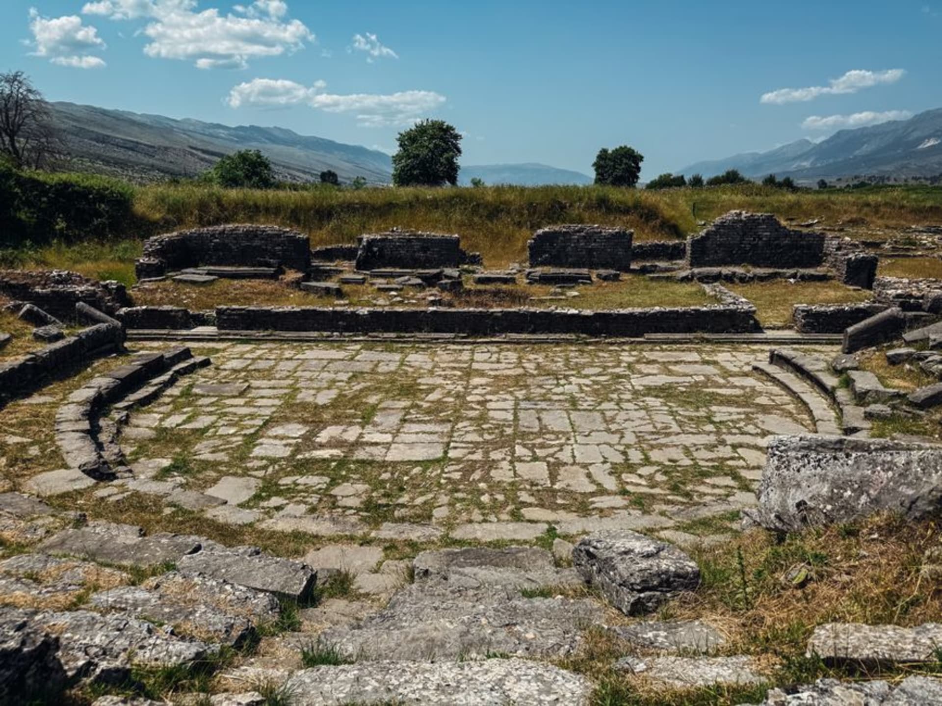 Ancient stone ruins of the Butrint archaeological site surrounded by dense forest beside a still lagoon in southern Albania.