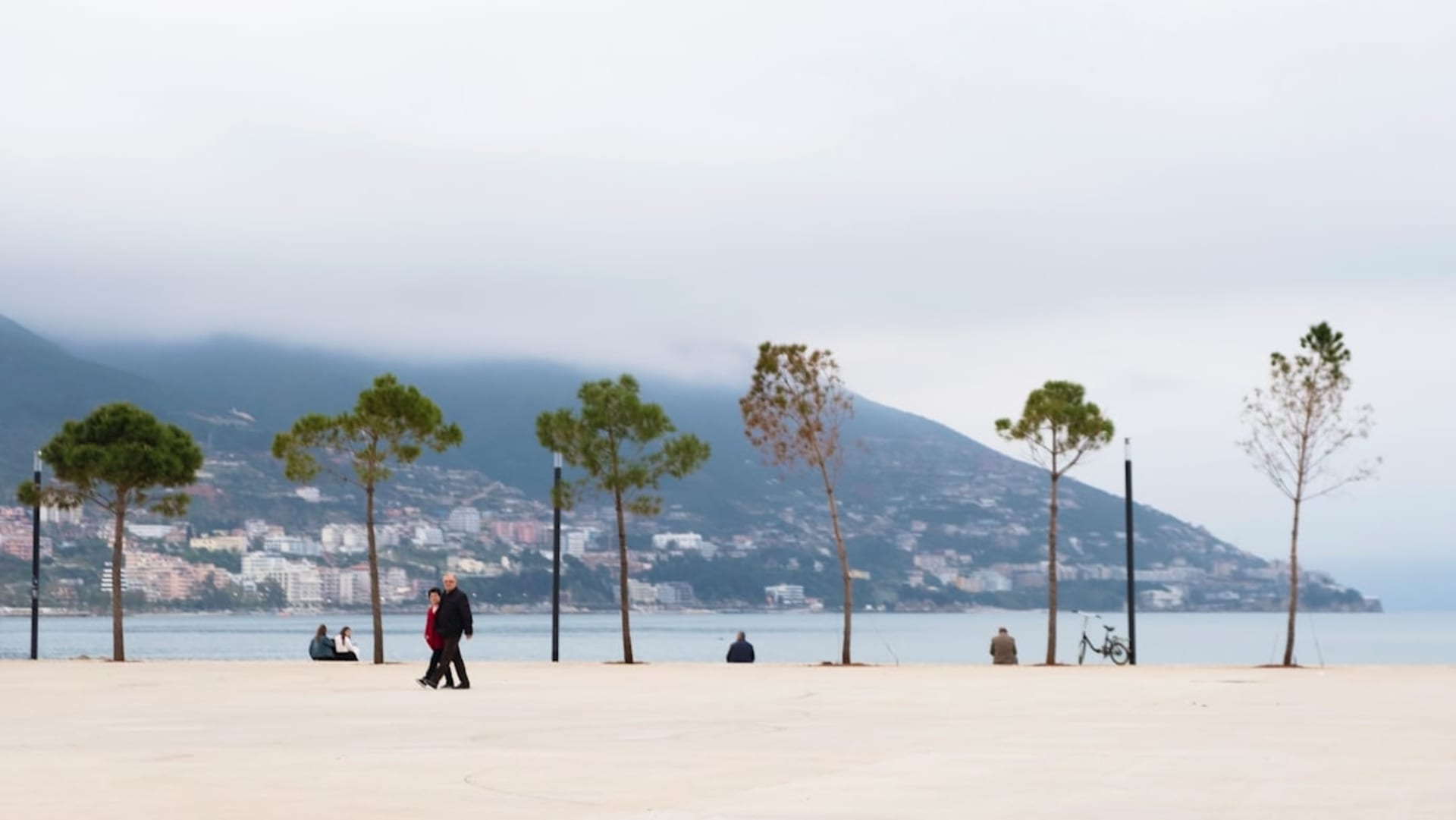 The long seafront promenade of Vlorë with palm trees and the Adriatic-Ionian meeting point visible in the bay beyond.