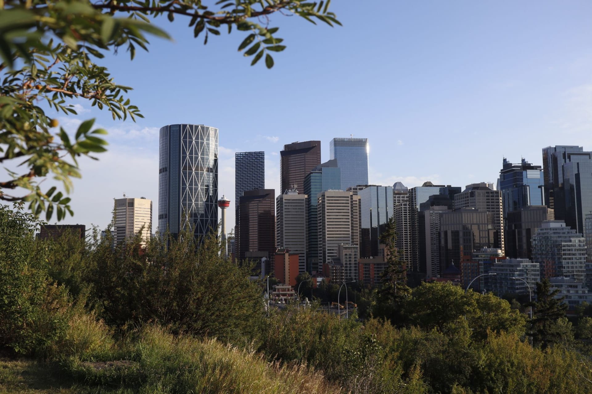 Calgary's downtown skyline at golden hour with the Rockies visible as a faint blue wall on the western horizon and the Bow River in the foreground