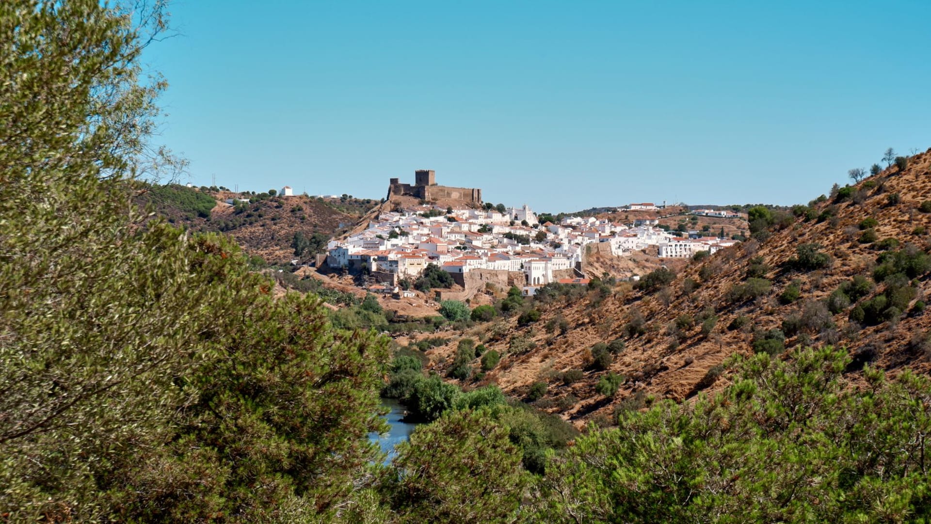 The white hilltop village of Mértola with its castle and former mosque-church rising above the dark waters of the Guadiana river