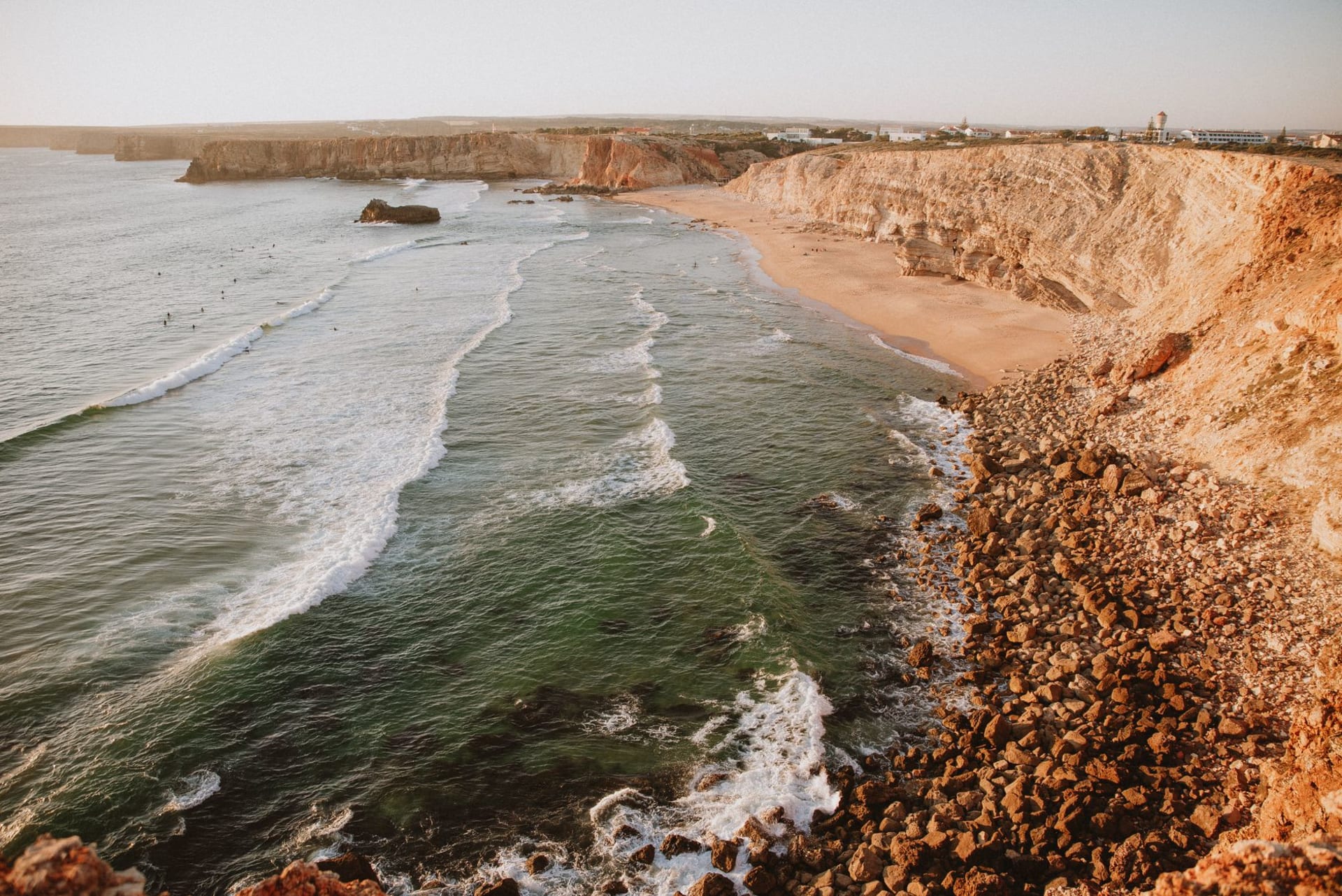 Cabo de São Vicente lighthouse perched on sheer black cliffs at the southwestern tip of Europe, orange sunset light raking across the Atlantic
