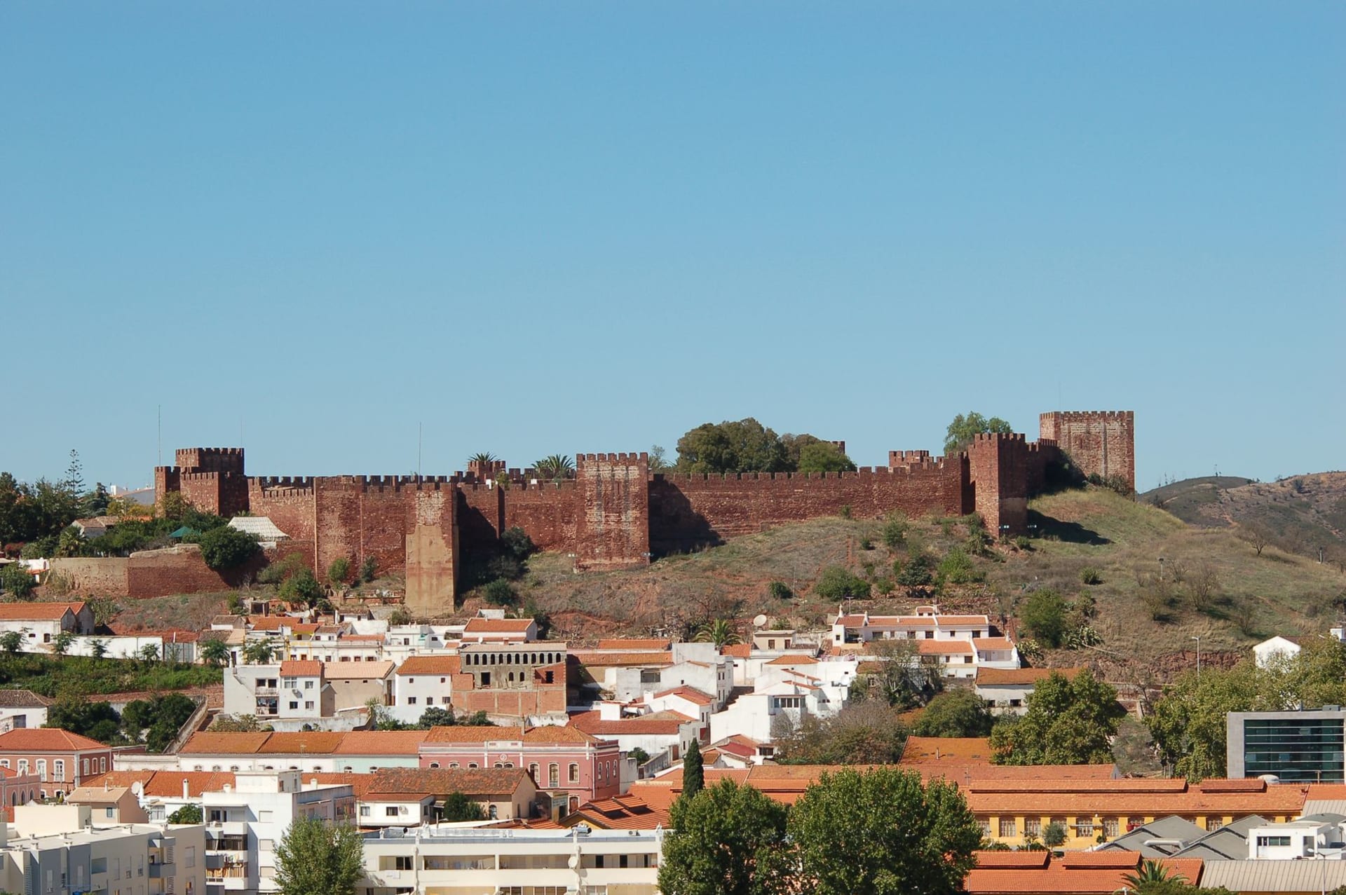 Silves red sandstone Moorish castle rising above whitewashed town buildings and orange trees, with the Arade river winding through the valley below