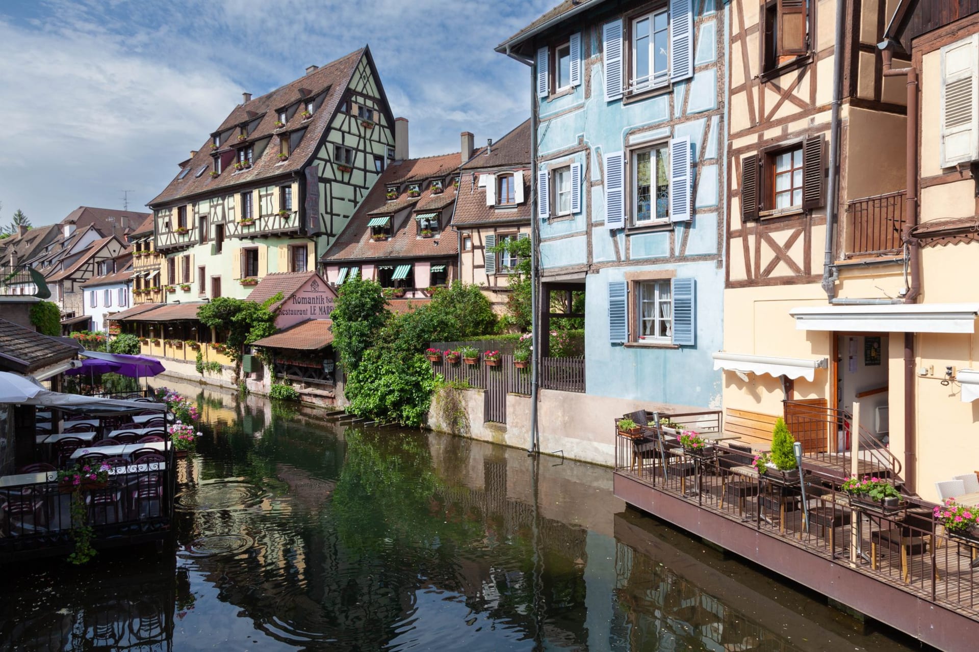 Medieval half-timbered buildings lining a canal in Colmar, their colorful facades reflected in the still water