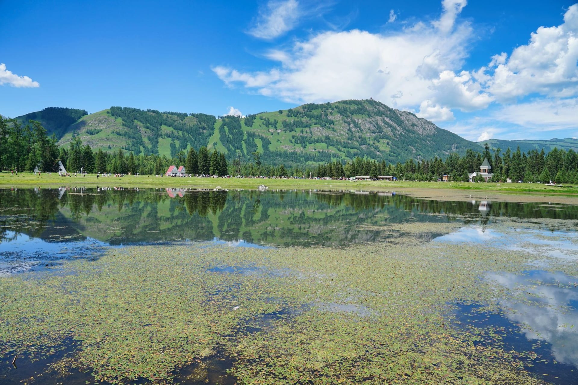 The Upper Multinskiye Lake reflecting pine forest and bare granite ridges in still morning water, a thin mist over the surface in early summer