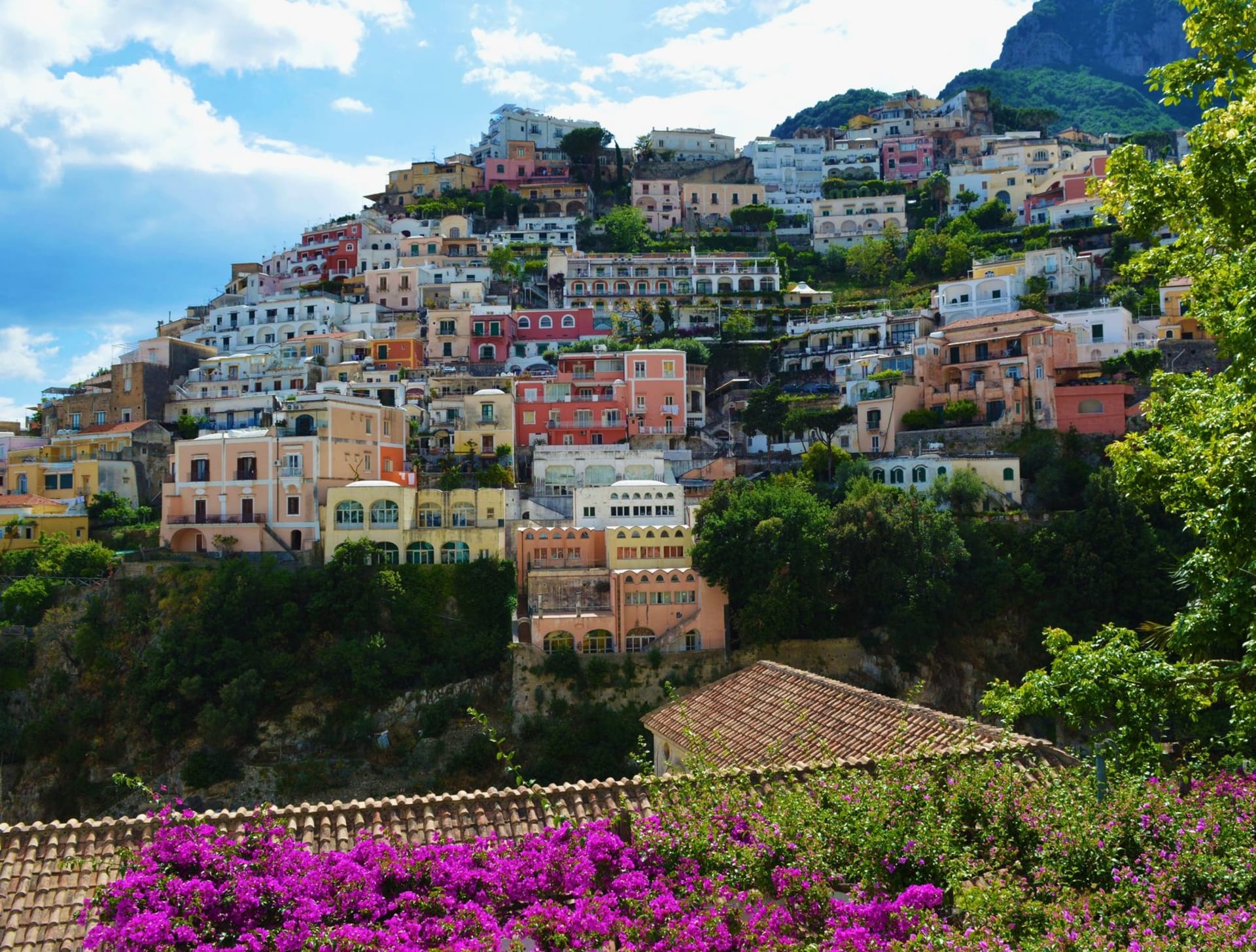 Positano's stacked pastel houses tumbling down the cliffside to a pebbly beach and turquoise bay, seen from the water