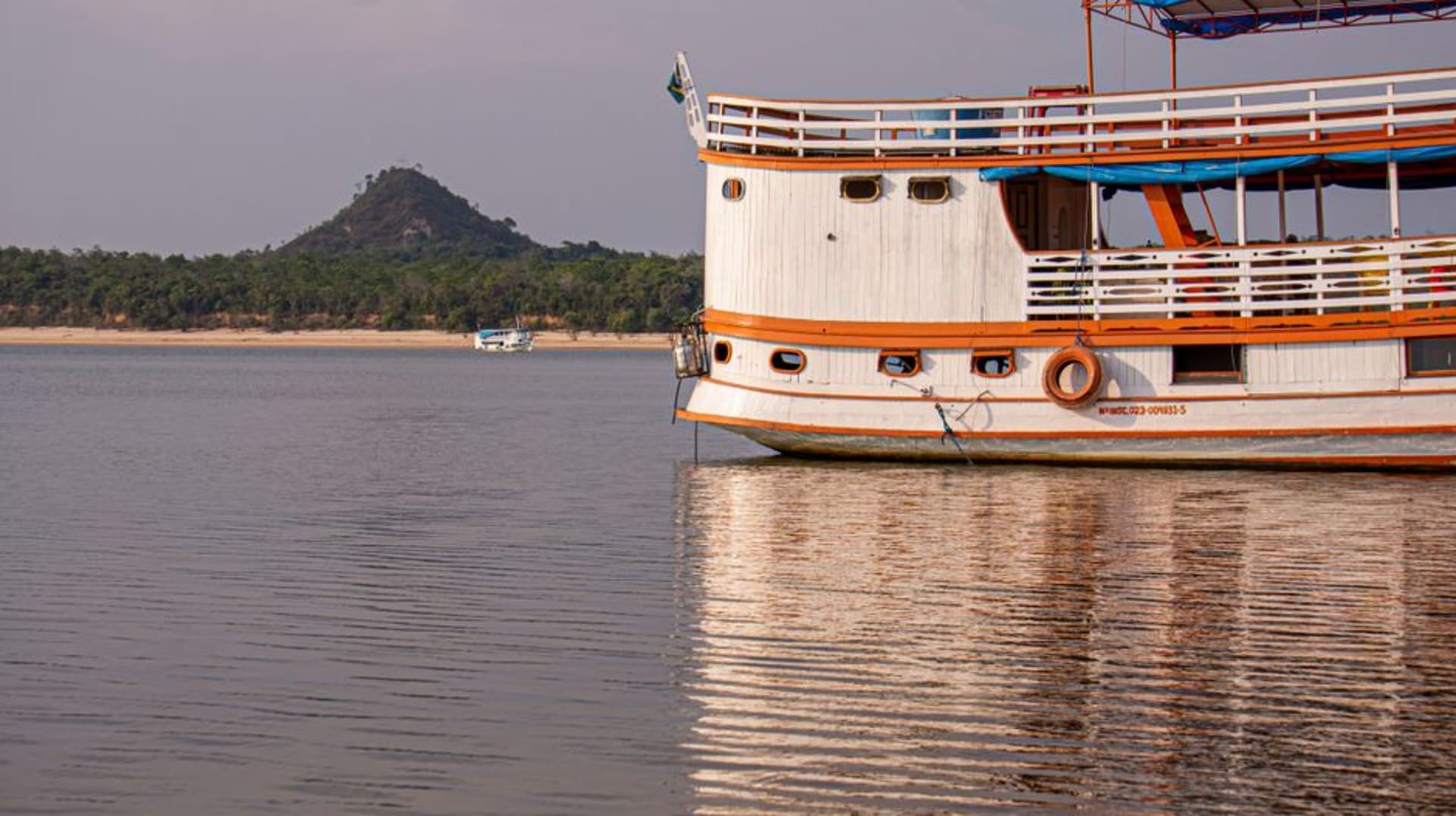 A wooden boat crossing the Guama River toward the forested shoreline of Ilha do Combu