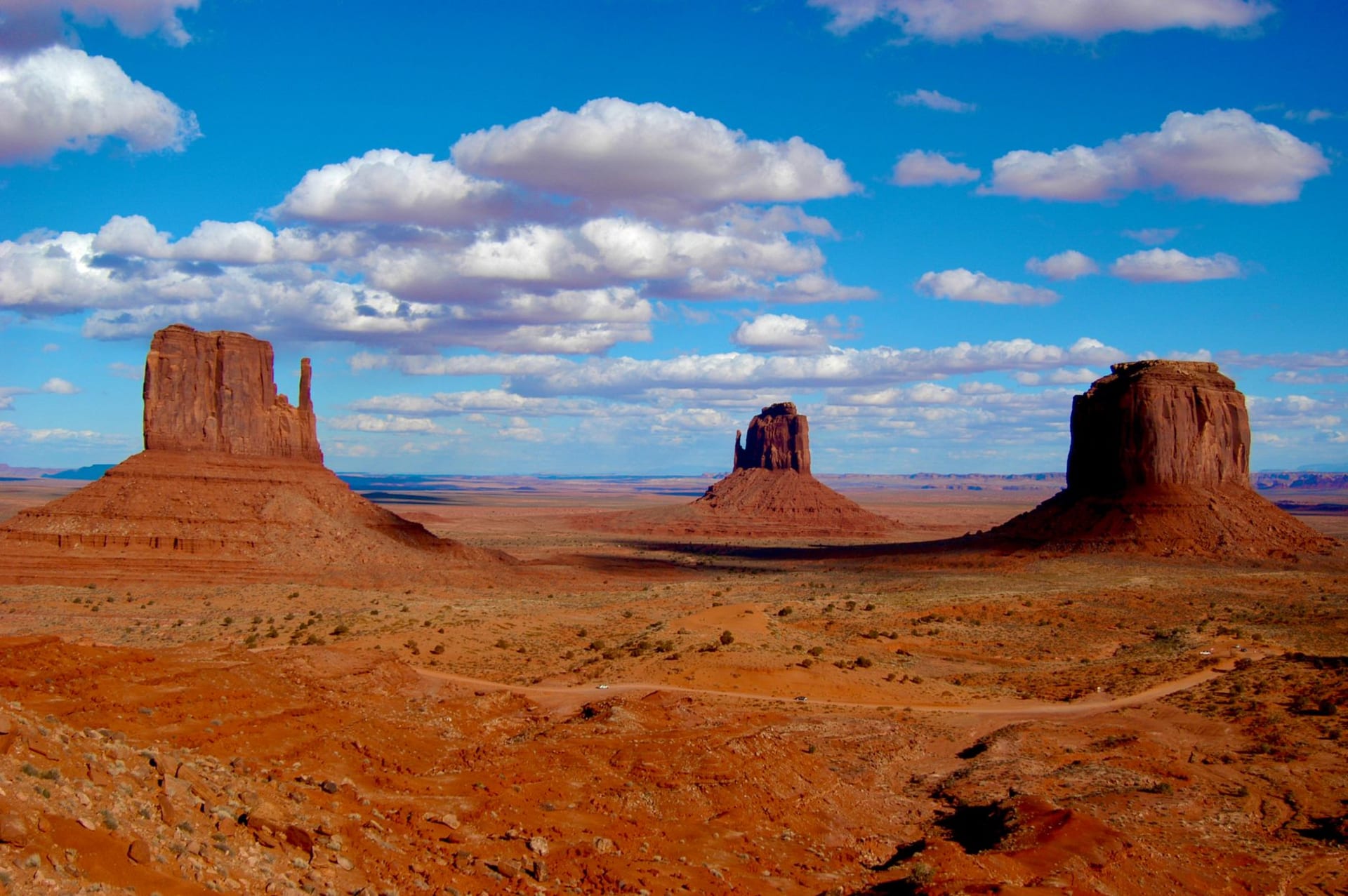 Dramatic landscape of Monument Valley's iconic buttes rising against a vibrant blue sky with scattered clouds