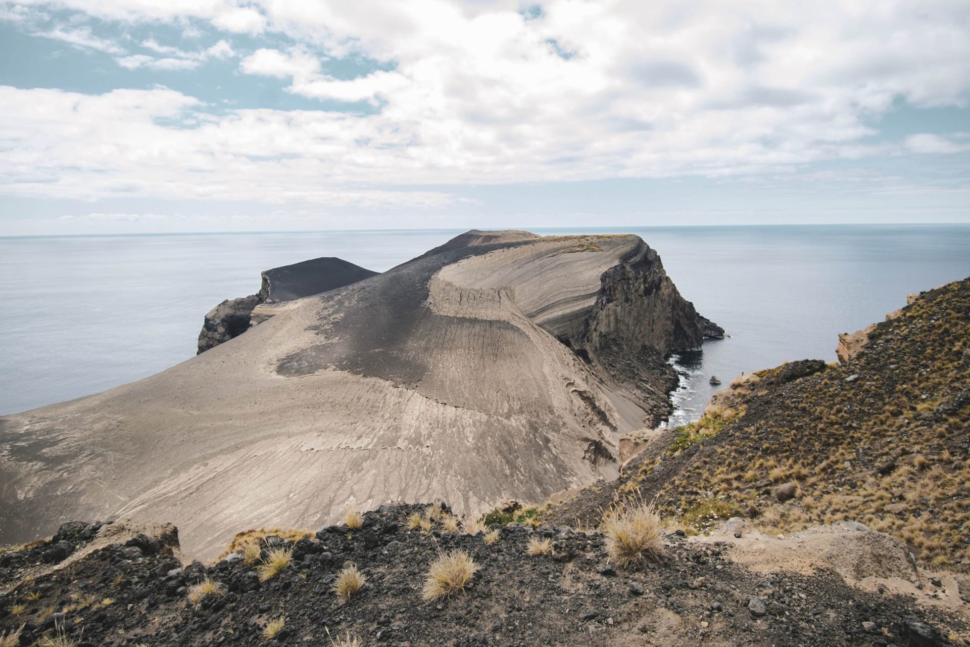 Le cône volcanique de l'île Barren émergeant de la mer avec un mince panache de fumée et un bateau de plongée au premier plan