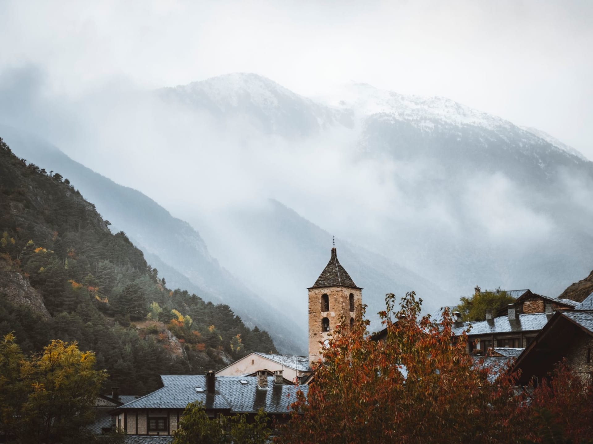 The Romanesque bell tower of Ordino's church emerging through morning mountain fog with stone village rooftops below