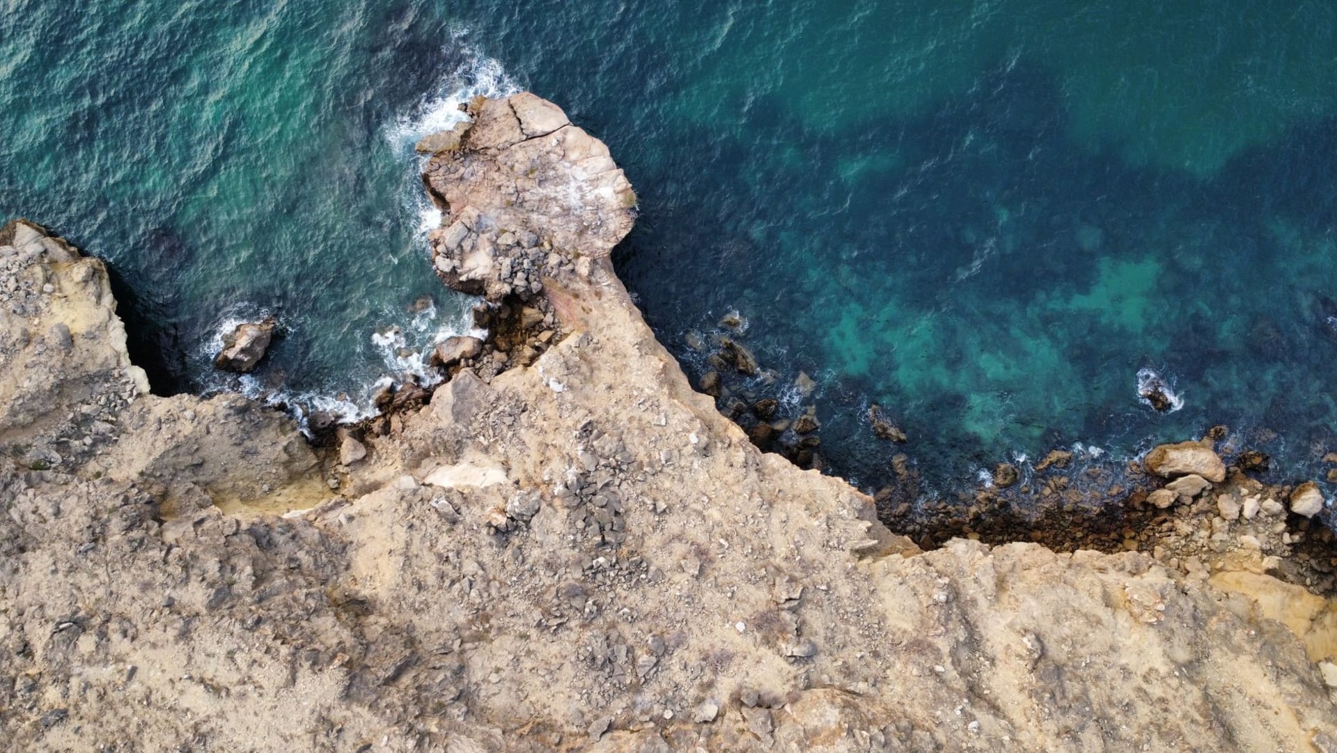Aerial view of Angola's rugged Atlantic coastline with turquoise waters crashing against rocky red cliffs
