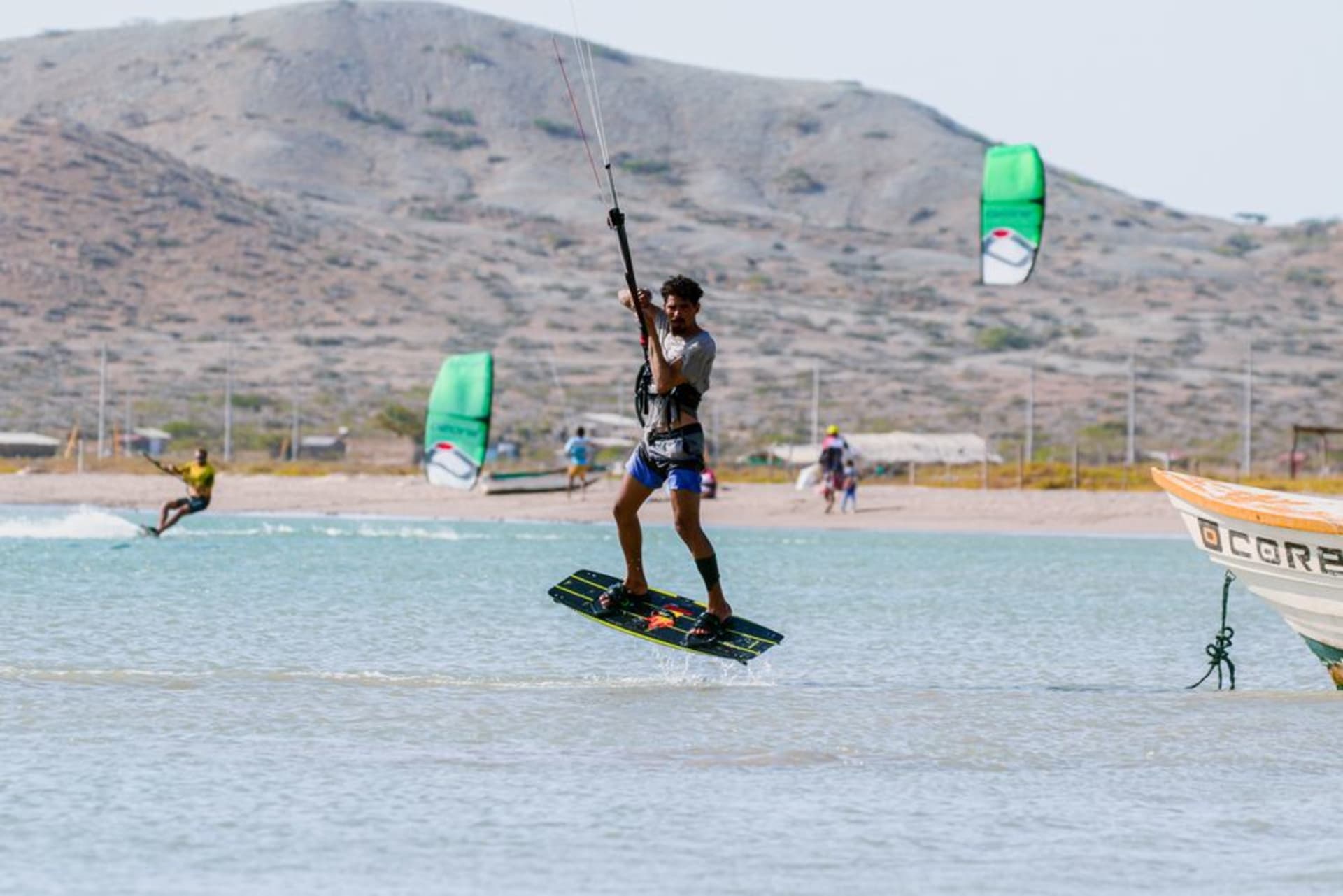 Red-clay cliffs above a long sandy beach at Cabo Ledo, Angola, with kitesurfers on the water