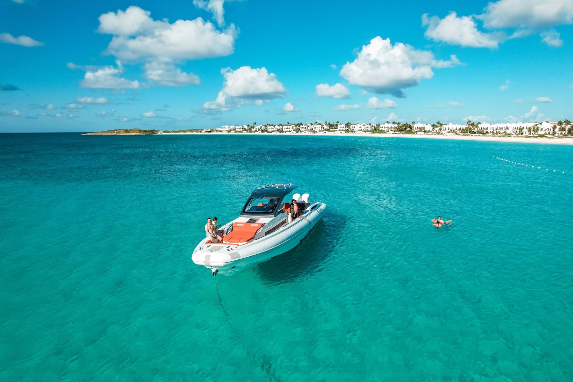 Aerial view of a motorboat cutting through impossibly clear turquoise water near an Anguilla white sand beach