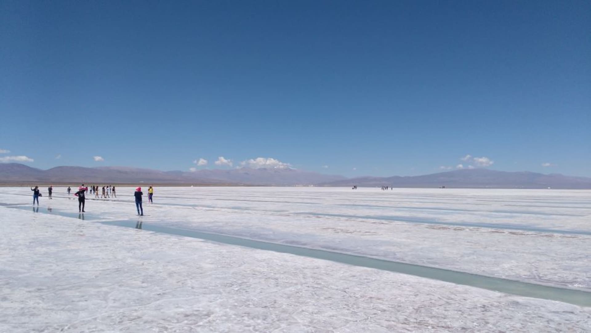 La cegadora extensión blanca de las Salinas Grandes con patrones hexagonales de costra de sal extendiéndose hasta picos andinos distantes