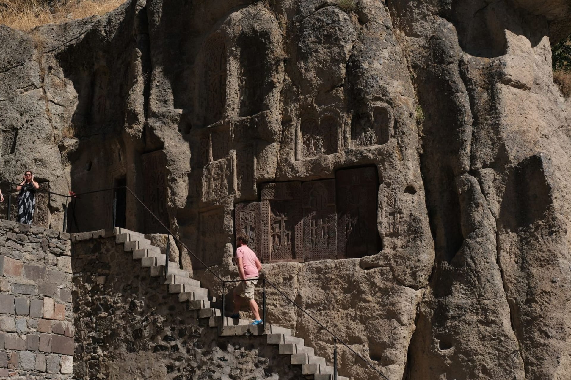 The stone facade of Geghard Monastery rising from sheer cliff walls in the Azat River gorge, golden light catching carved khachkars and medieval stonework against a sky of deep Armenian blue.