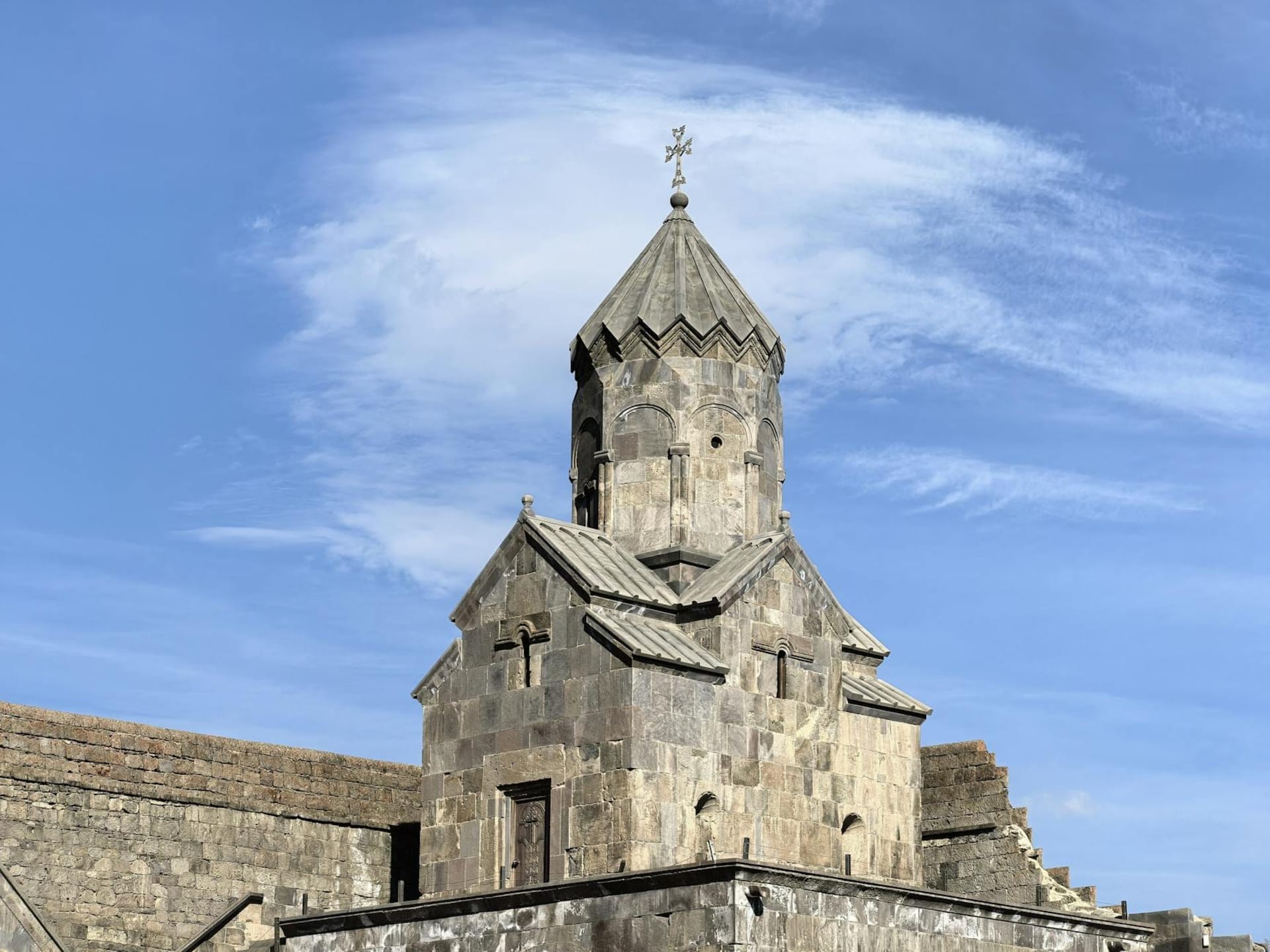 Tatev Monastery perched on a dramatic basalt promontory above the deep Vorotan River gorge, its medieval stone towers rising against a pale Armenian sky