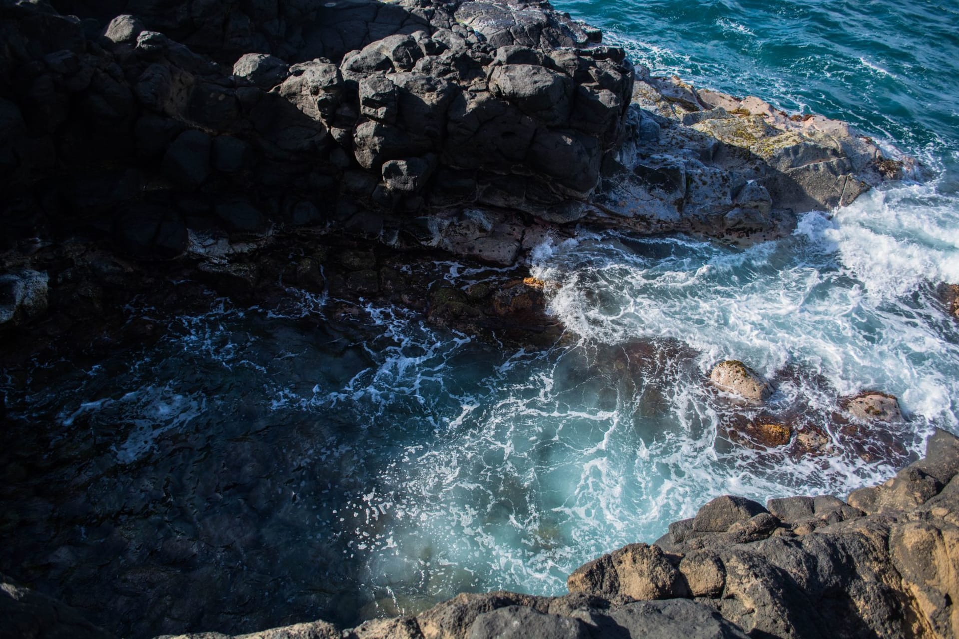 La piscina natural Conchi en Aruba — una piscina turquesa circular rodeada de roca volcánica negra con olas atlánticas rompiendo en la pared exterior